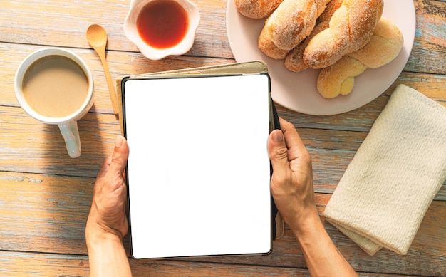 El desayuno y la tableta en la mano, la rutina de la mañana, la mano de la mujer europea sostiene el café o el té.