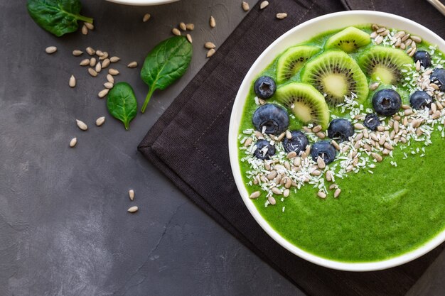 Desayuno tazón de batido verde con kiwi, arándanos y semillas de girasol sobre fondo de hormigón gris