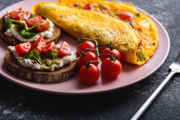 Desayuno con tortilla y pan de grano con queso crema, pesto y tomates cherry en un primer plano de placa rosa