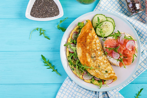 Desayuno. Tortilla con rábano, rúcula verde y sandwich con salmón en plato blanco