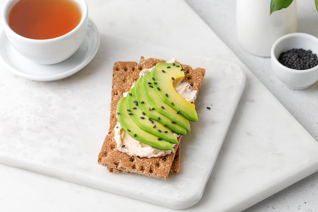 Desayuno con tostadas de aguacate con pan integral con semillas de sésamo negro sobre tablero de mármol. Taza de té.