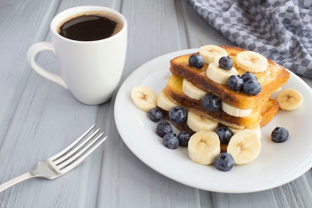 Desayuno: tostadas francesas con arándanos, plátano, miel y café sobre el fondo de madera gris. De cerca.