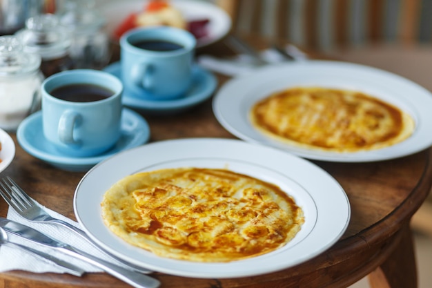 Desayuno tradicional balinesse con dos tazas azules de bebida caliente en la mesa de madera.