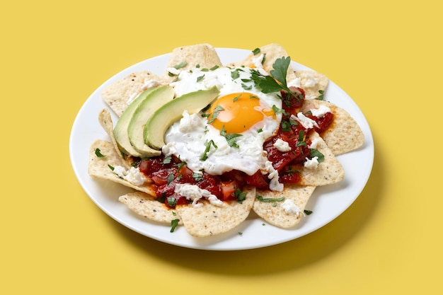 Desayuno tradicional mexicano chilaquiles rojos con huevo sobre fondo amarillo