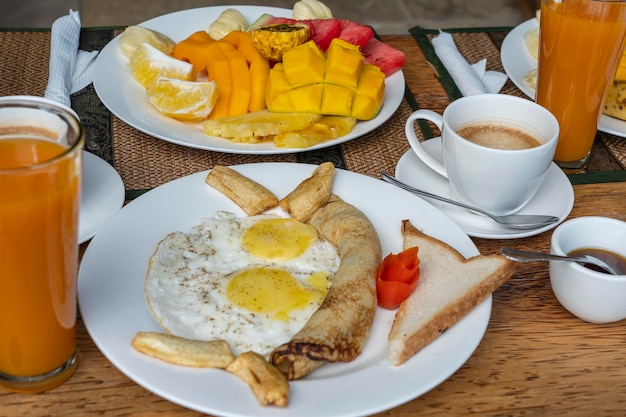 Desayuno tropical de café de frutas y huevos revueltos y tortitas de plátano para dos en la playa cerca del mar