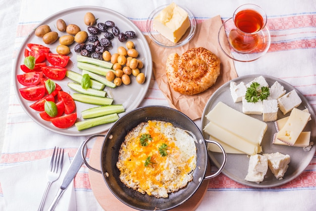 Foto desayuno turco tradicional: huevos fritos, verduras frescas, aceitunas, queso, pasteles y té