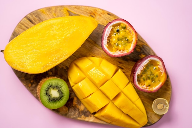 Desayuno vegano saludable de frutas crudas. Primer plano de mango fresco en rodajas, kiwi, maracuyá, longan sobre tabla de cortar de madera. Vista superior, endecha plana. Frutas exóticas tropicales sobre fondo rosa.