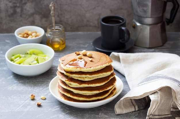 Desayuno vegetariano de panqueques, café, miel, nueces y frutas.