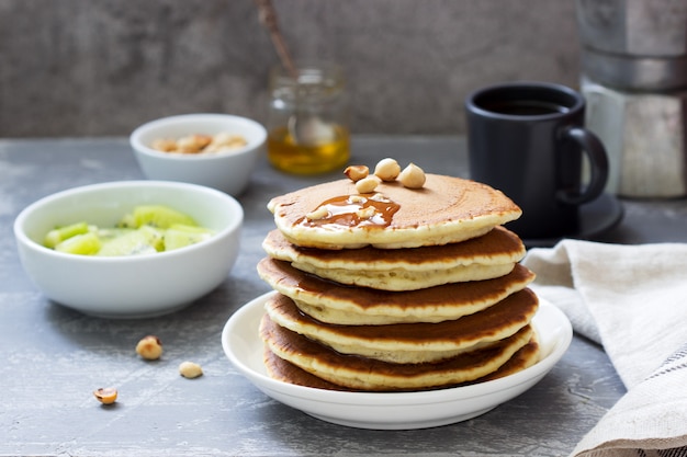 Desayuno vegetariano de panqueques, café, miel, nueces y frutas.