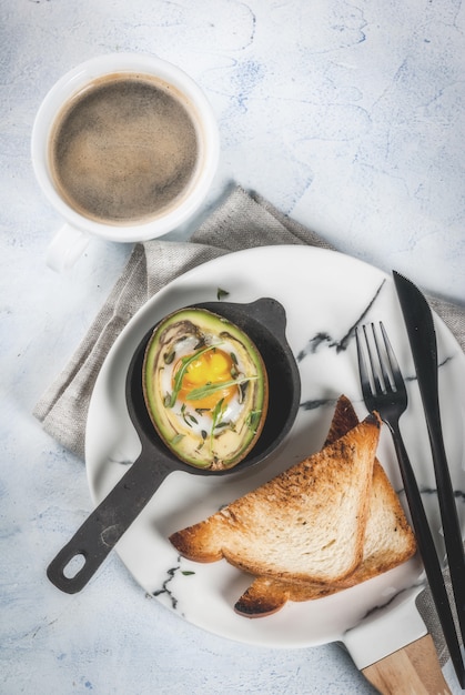 Desayuno vegetariano saludable Dieta Aguacate al horno con huevo y ensalada fresca de tostadas de rúcula y mantequilla En una placa de mármol blanco, una mesa de concreto ligero