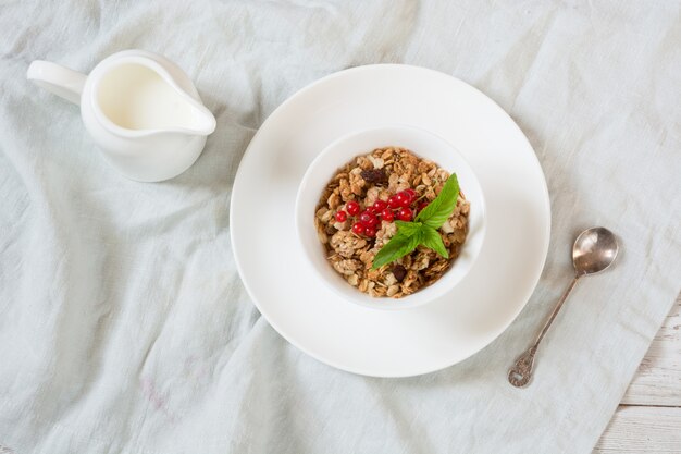 Desayuno de verano de granola, muesli con jarra de leche con decoración de grosella roja en tablero de madera clara. Vista superior.