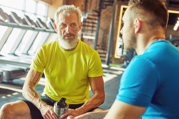 Descansando después del entrenamiento centrado en el hombre de mediana edad en ropa deportiva sosteniendo una botella de agua y hablando