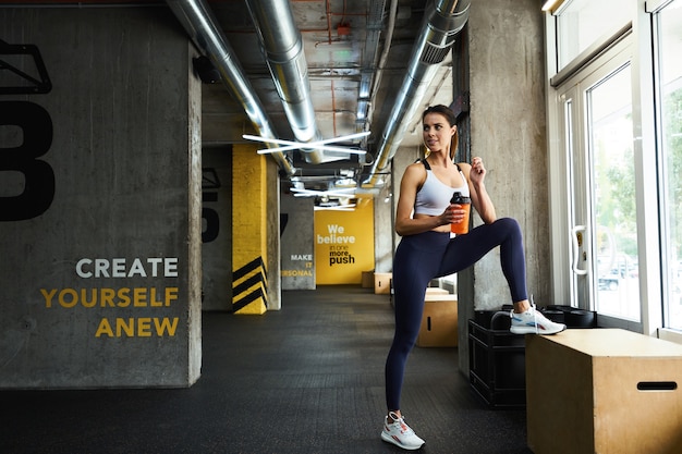 Descansando después del entrenamiento de longitud completa de una joven y bella mujer fitness en ropa deportiva sosteniendo la botella