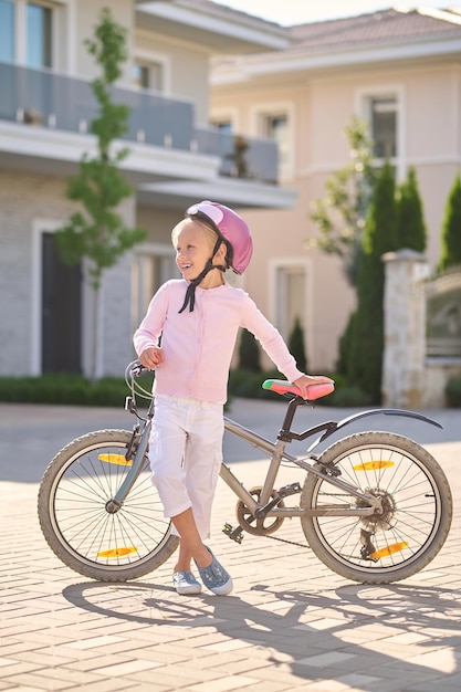 Descansando. Una niña en casco de pie cerca de la bicicleta.