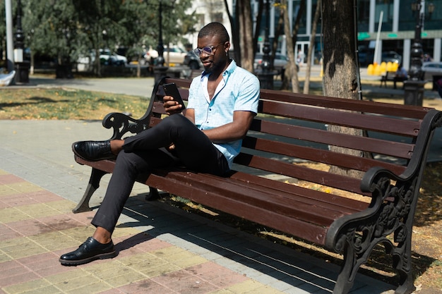 descansando o homem africano no banco com o celular