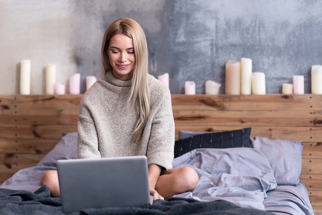 Descansar en casa. Encantado de hermosa mujer joven sentada en la cama y usando la computadora portátil mientras se relaja.