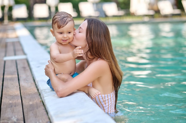 Descansar. Una mujer joven que sostiene a su hijo y se siente bien mientras nada en una piscina.