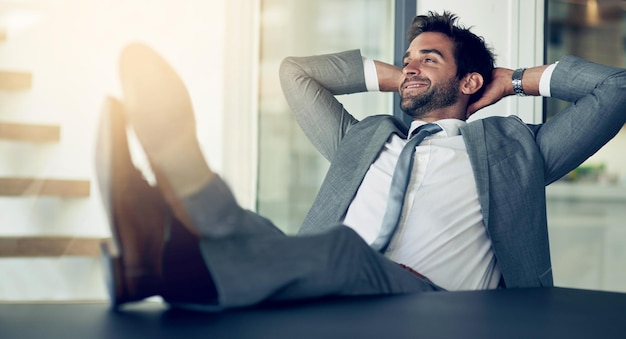 Foto descanse la confianza y el hombre de negocios con las manos detrás de la cabeza después de terminar el proyecto en la oficina relájese tranquilo y feliz empleado profesional en un descanso con una tarea exitosa en el lugar de trabajo