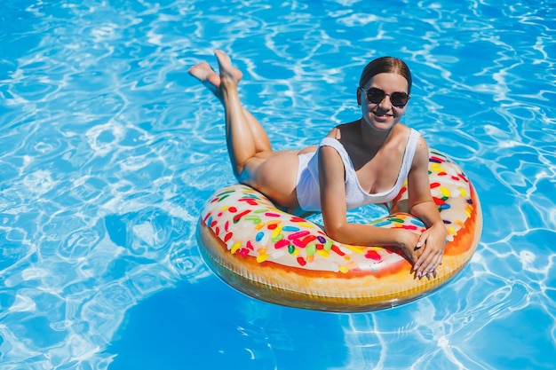Foto descanse na piscina jovem feliz em óculos de sol de maiô e anel de borracha inflável flutuando na água azul férias de luxo de verão na piscina do spa resort