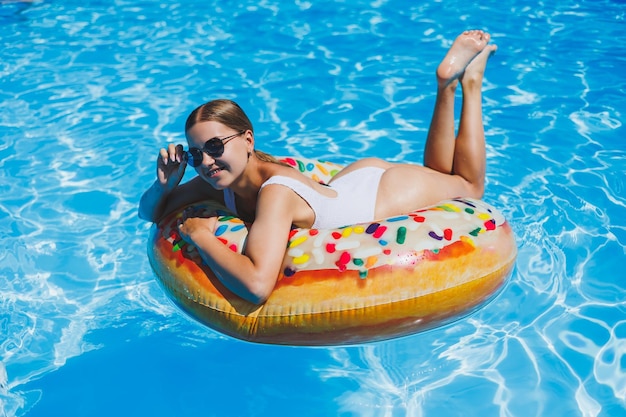 Descanse na piscina Jovem feliz em óculos de sol de maiô e anel de borracha inflável flutuando na água azul Férias de luxo de verão na piscina do spa resort