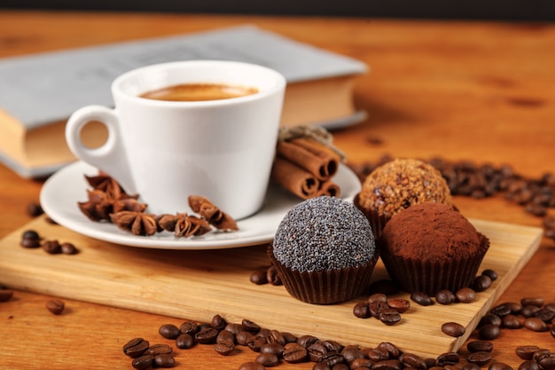 Foto descanso. café caliente en taza y tortas en una tabla de madera. espresso, libro abierto, granos de café, canela, anís.