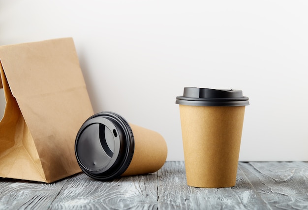 Un descanso y un costo para llevar tazas de café de papel con bolsa de almuerzo sobre fondo de madera