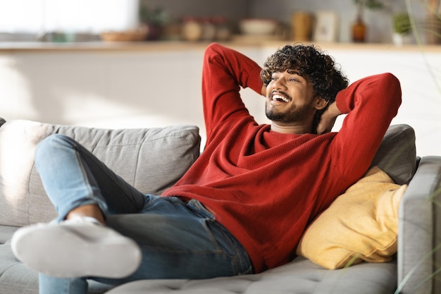 Descanso doméstico relaxado jovem indiano recostando-se no sofá em casa