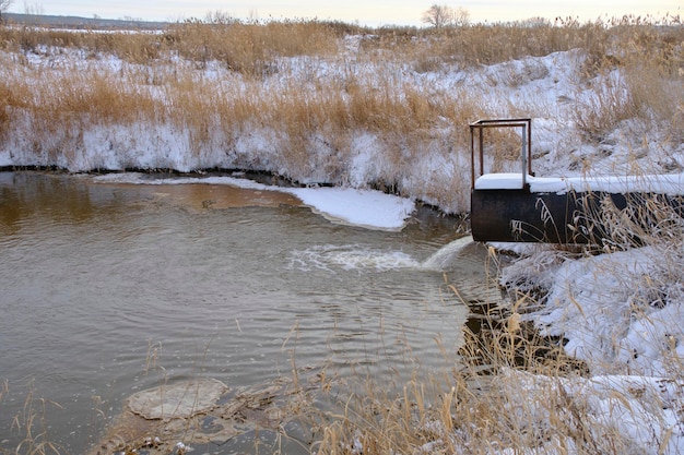 Descarga de aguas residuales de la tubería al río en invierno Contaminación y ecología del río