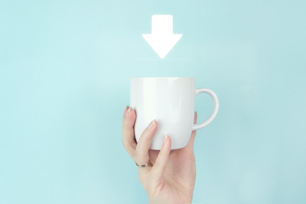 Descargar concepto de día. Cerrar la mano de la chica mantenga la taza de café de la mañana con el icono de signo de descarga sobre fondo azul.