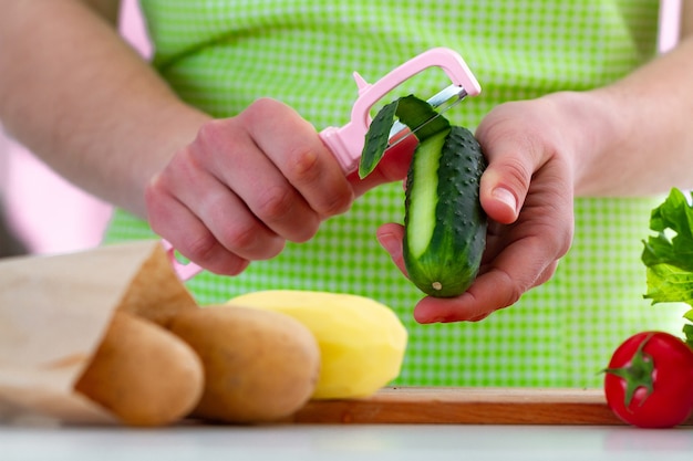 Descascar o pepino com um descascador para cozinhar pratos frescos e saladas de legumes em casa.