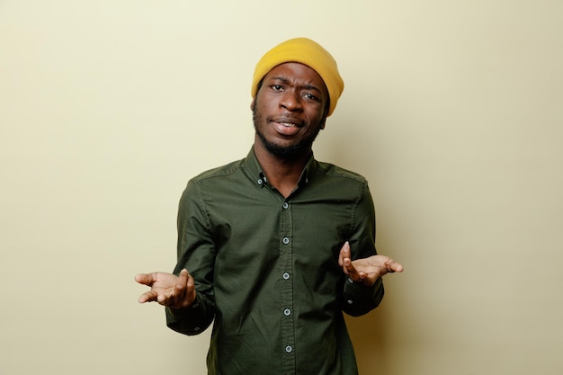 Descontento extendiendo las manos joven afroamericano con sombrero con camisa verde aislado sobre fondo blanco.