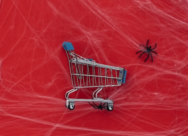 Descontos de Halloween, compras. Carrinho de supermercado em vermelho com teias de aranha e aranhas. Decoração de halloween