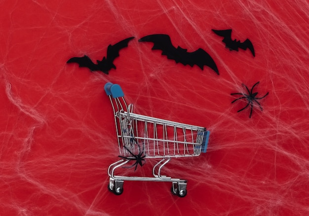 Descontos de Halloween, compras. Carrinho de supermercado em vermelho com teias de aranha, morcegos e aranhas. Decoração de halloween