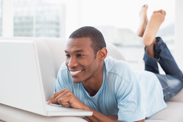 Descontraído casual homem afro com laptop deitado no sofá