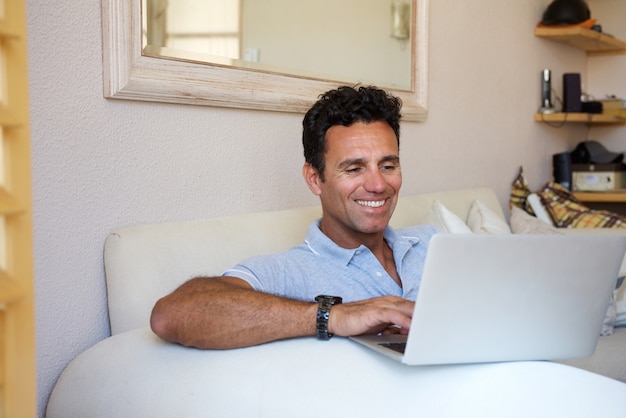 Foto descontraído homem envelhecido médio sorrindo com laptop em casa