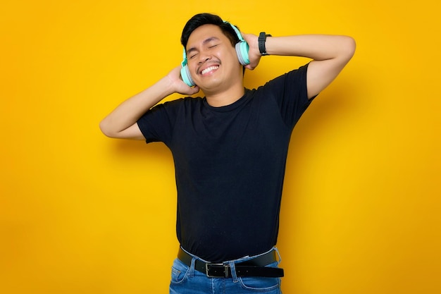 Descontraído jovem asiático em camiseta casual ouvindo música em fones de ouvido isolados em fundo amarelo Conceito de estilo de vida de emoções de pessoas