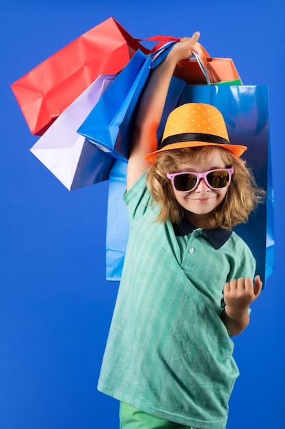 Descuentos y ventas Niño feliz niño con bolsas de compras Niño con bolsas de compras posando en estudio azul