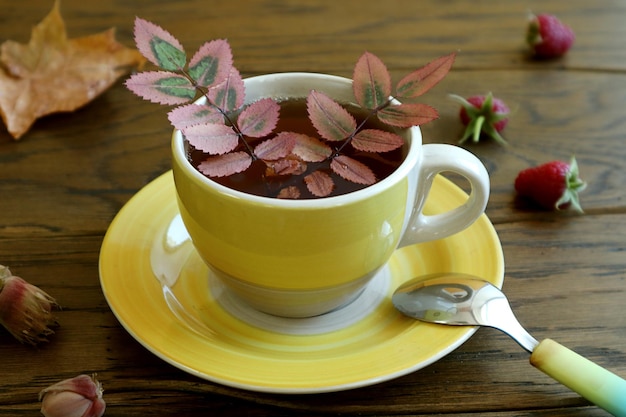 Desea una cálida mañana de otoño una taza de té amarilla que contiene hojas de otoño frambuesas nueces en una mesa de madera cerrada