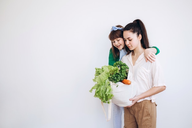 Desembalaje de una bolsa ecológica de verduras frescas y verduras después de la compra por parte de dos niñas. Concepto de alimentación saludable.