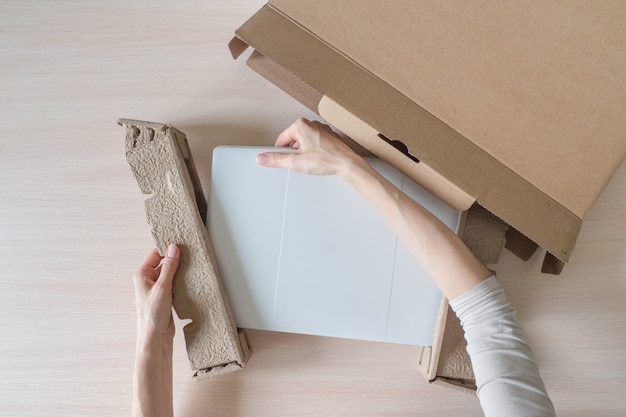 Foto desembalar una nueva computadora portátil de una caja de cartón. las manos abren la caja. desempacando el paquete recibido