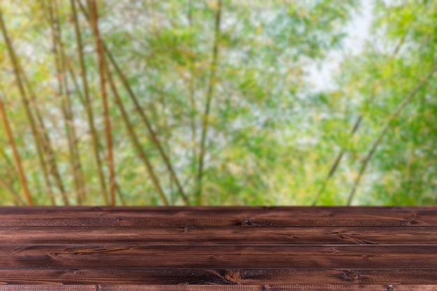 Desenfoque de bosque de arboleda de bambú de árbol verde con espacio de madera en primer plano para el fondo de publicidad de montaje de productos.