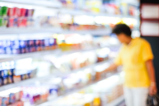 Desenfoque a la gente de compras en el estante del producto en el fondo del supermercado