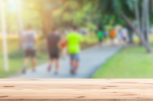 Desenfoque de gente corriendo en el parque con la parte superior de la mesa de madera en primer plano para el fondo del montaje de productos deportivos