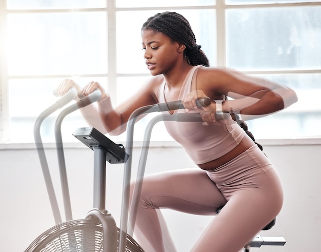 Desenfoque de movimiento bicicleta de ejercicio y mujer negra en el gimnasio para entrenamiento cardiovascular y movimiento con energía de velocidad y motivación Fitness girl máquina de ciclismo estacionaria y bicicleta de aire bienestar y acción