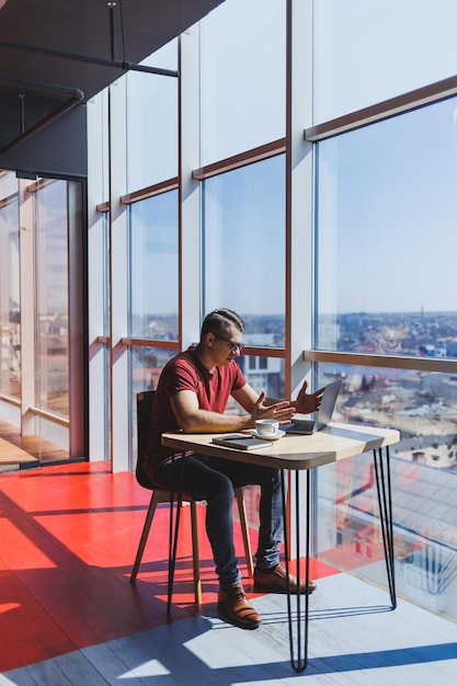 Desenvolvedor de software inteligente sentado na área de trabalho em um espaço de coworking com laptop e criando uma ideia de publicação usando netbook para mensagens e redes durante o trabalho freelance