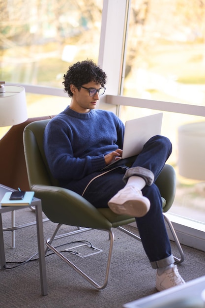 Desenvolvedor jovem latino-americano sério usando laptop online trabalhando em novo projeto de software