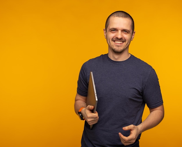 Desenvolvedor ou freelancer segurando laptop e vestindo uma camiseta cinza em fundo laranja