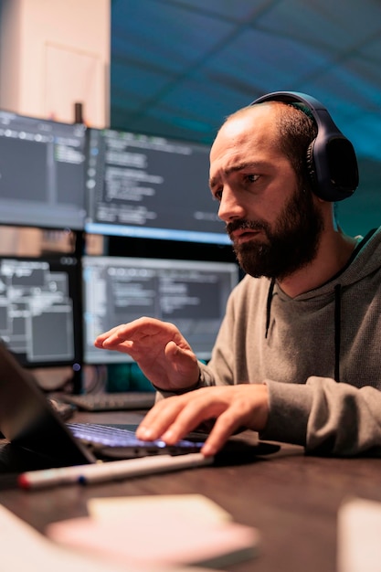 Desenvolvedor web masculino escrevendo código e ouvindo música em fones de ouvido, usando script de inteligência artificial para programar big data no laptop. Servidor de programação na janela do terminal.