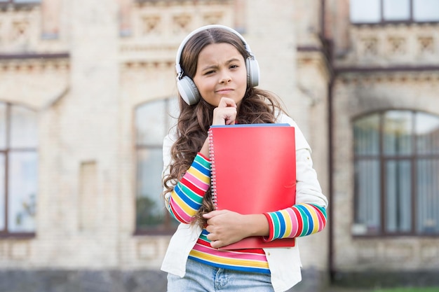 Desenvolvendo habilidades de escuta eficazes Garotinha séria ouvindo aula de áudio em fones de ouvido Criança pequena bonita pratica compreensão auditiva Faça anotações enquanto ouve para reter o vocabulário