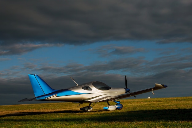 Foto desfocar pequeno avião leve em um campo de grama em um fundo de nuvens azuis